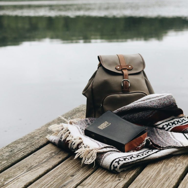 Women’s Leadership Retreat Costa Rica A backpack next to a blanket and a book on a wooden dock by a calm lake.
